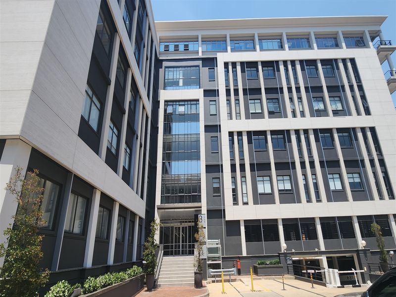 Modern multi-story office building facade featuring a contemporary glass and concrete design with a prominent entrance and integrated parking access.