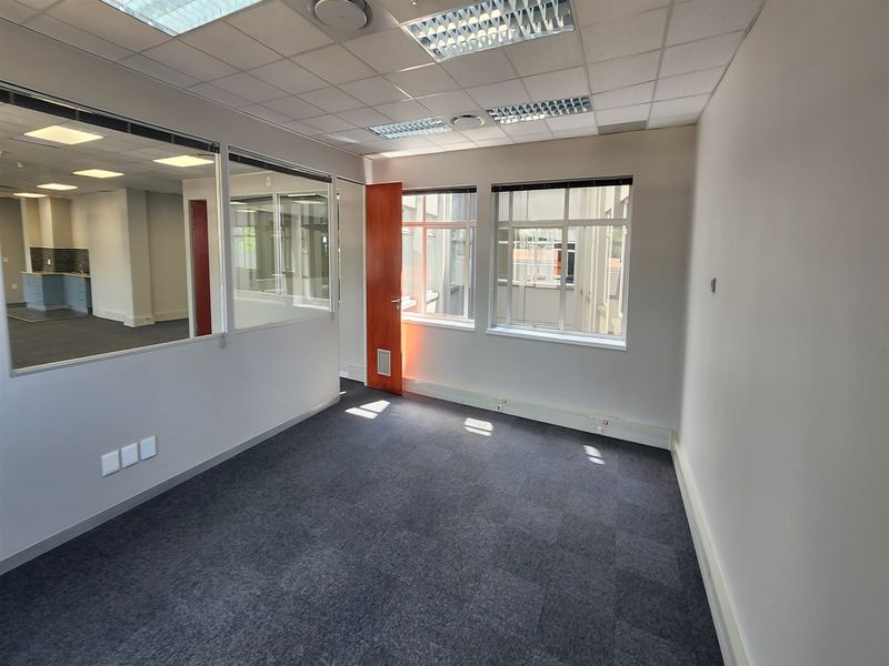 A bright, empty office space featuring carpet tiles, glass partition walls, and a suspended ceiling with recessed lighting, ideal for a professional workspace.