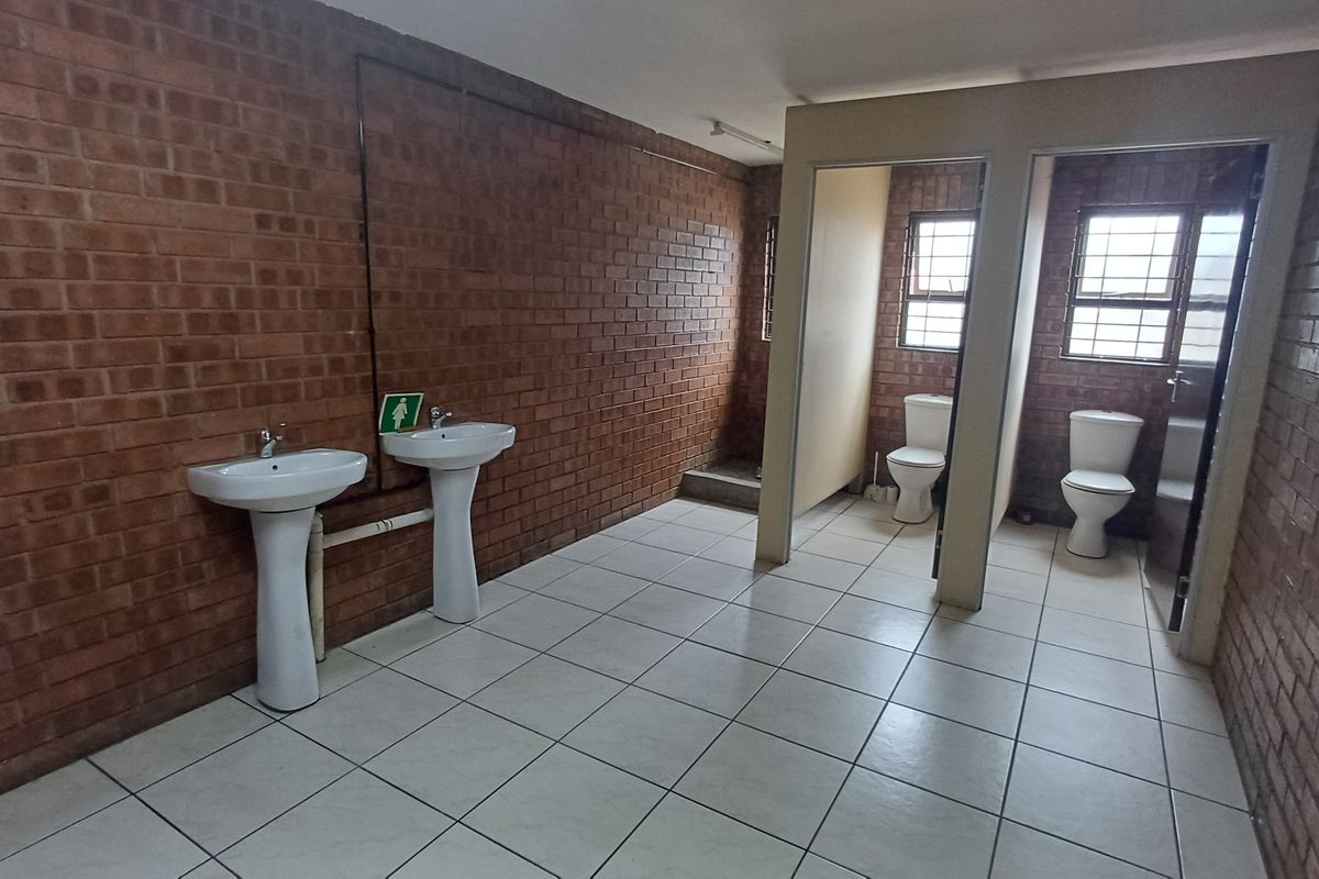 Functional industrial restroom facility featuring exposed brick walls, two pedestal basins, and two private toilet cubicles with tiled flooring.