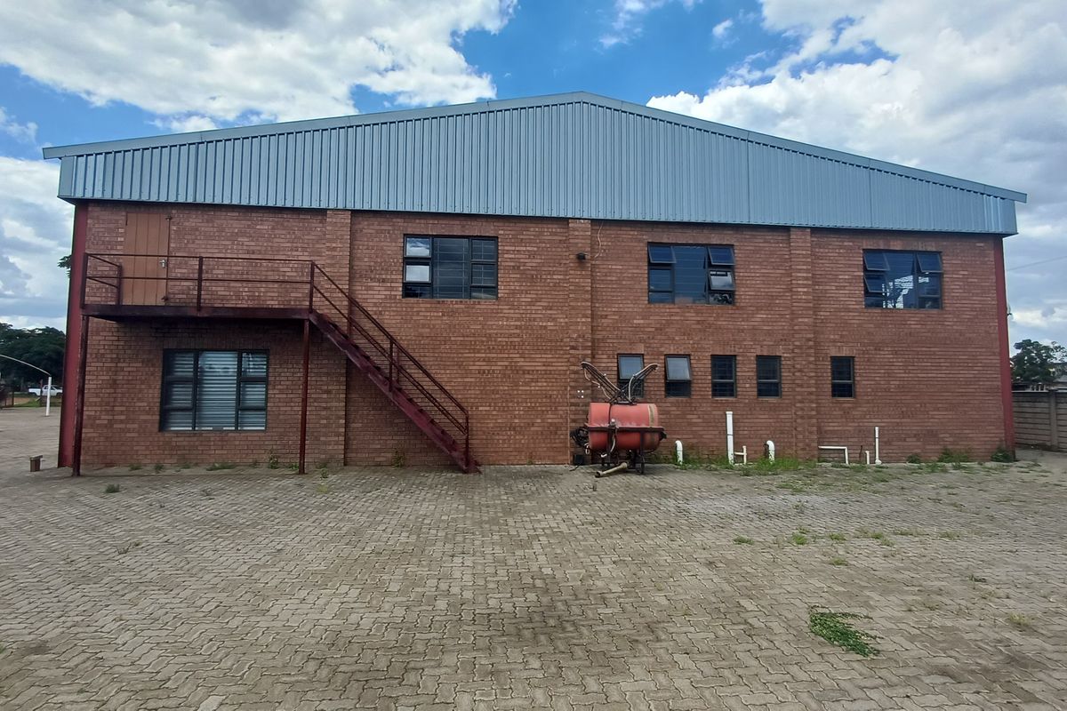 Industrial warehouse building featuring exposed brick facade, metal roof, external steel staircase, and paved yard area.