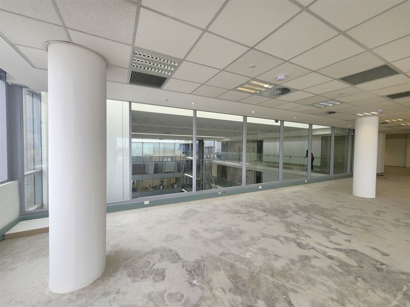 An open-plan office space featuring large floor-to-ceiling windows, suspended ceilings with integrated lighting, and unfinished flooring ready for custom fit-out.