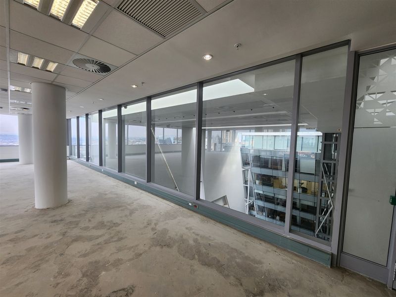 A spacious, empty office area featuring large floor-to-ceiling windows, a suspended ceiling with recessed lighting, and an open-plan layout ready for fit-out.