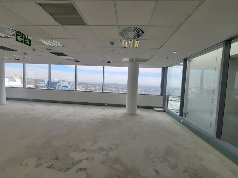 An empty, open-plan office space featuring floor-to-ceiling windows with expansive city views, suspended ceilings, and recessed lighting.