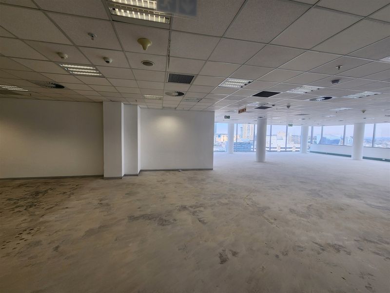 Spacious open-plan office area featuring large floor-to-ceiling windows with city views, suspended ceilings, and exposed concrete flooring ready for new finishes.