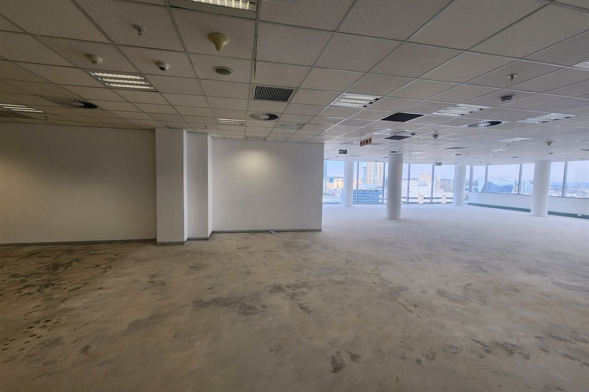 Spacious open-plan office area featuring large floor-to-ceiling windows with city views, suspended ceilings, and exposed concrete flooring ready for new finishes.