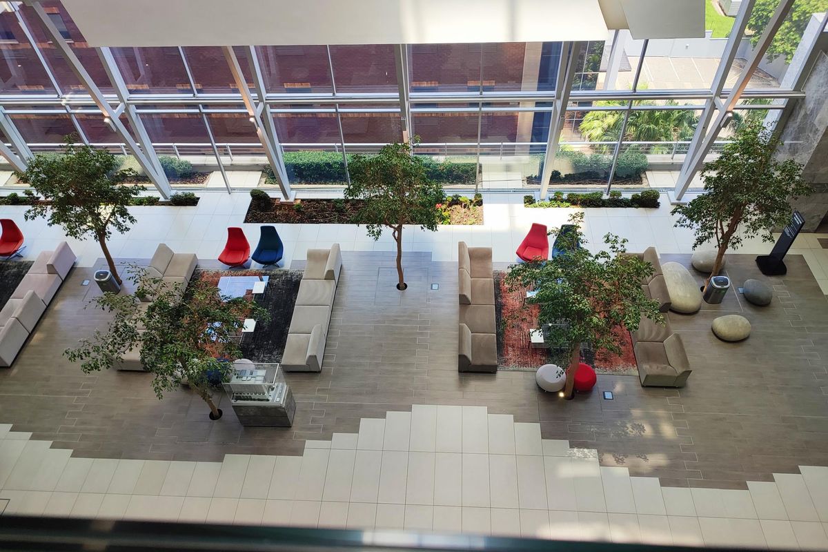 Spacious modern office atrium featuring floor-to-ceiling glass windows, tiled flooring, and integrated indoor landscaping for a bright, professional environment.