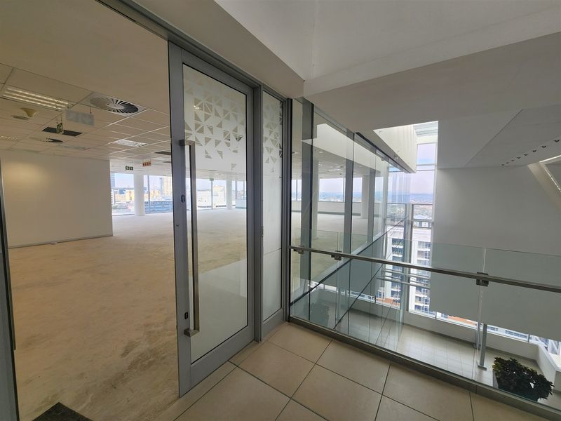 Modern open-plan office space featuring glass partitions, suspended ceilings, and large windows offering expansive city views.