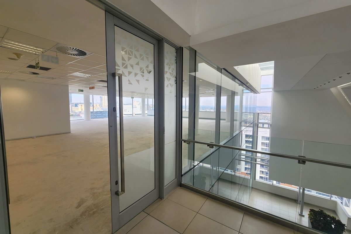Modern open-plan office space featuring glass partitions, suspended ceilings, and large windows offering expansive city views.