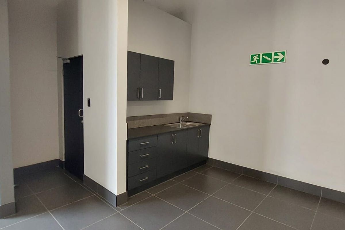A functional kitchenette area featuring dark cabinetry, a stainless steel sink, and tiled flooring within a commercial retail space.