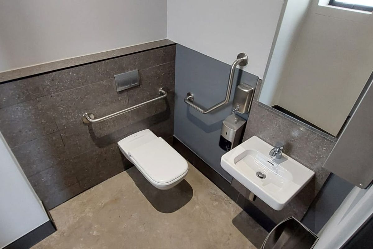 A modern, accessible restroom featuring a wall-mounted toilet, a compact basin, and stainless steel grab rails for accessibility.