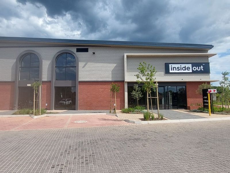Modern retail building exterior featuring a combination of brick and rendered facade, large arched windows, and a paved parking area.