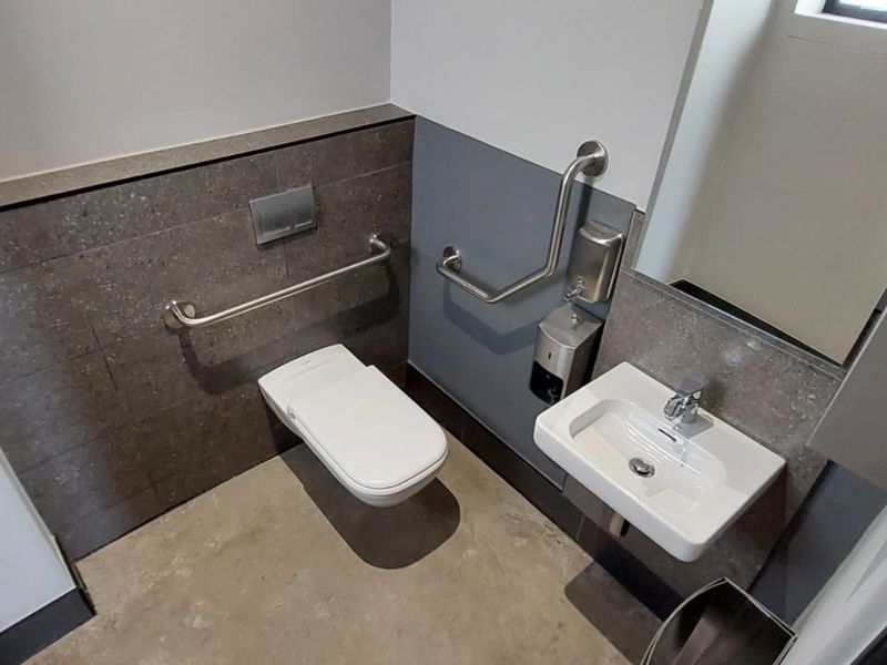 A modern, accessible restroom featuring a wall-mounted toilet, a compact basin, and stainless steel grab rails for accessibility.