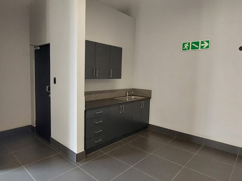 A functional kitchenette area featuring dark cabinetry, a stainless steel sink, and tiled flooring within a commercial retail space.