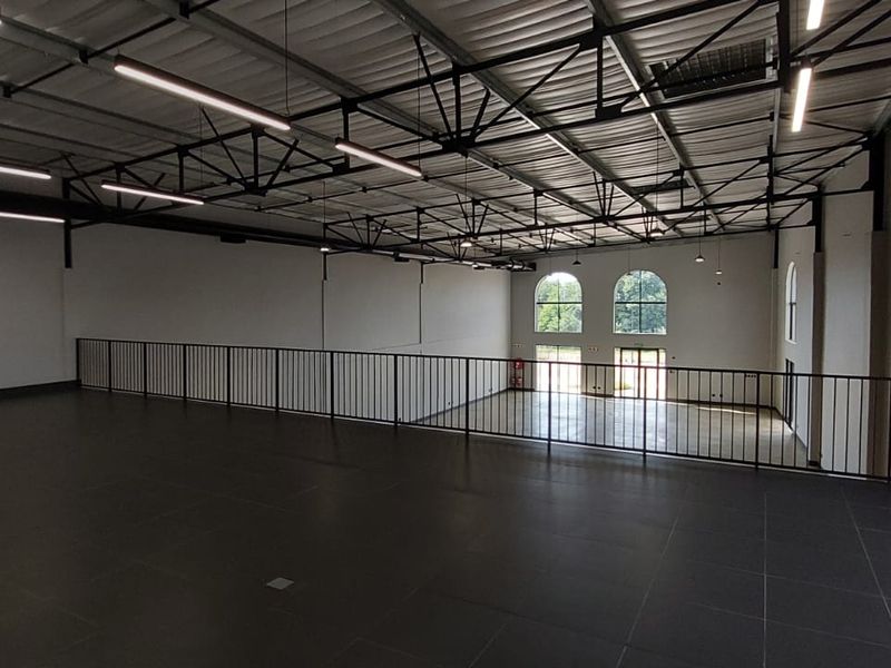 Spacious open-plan mezzanine level featuring tiled flooring, industrial-style exposed ceiling trusses, and modern linear lighting fixtures overlooking the ground floor.