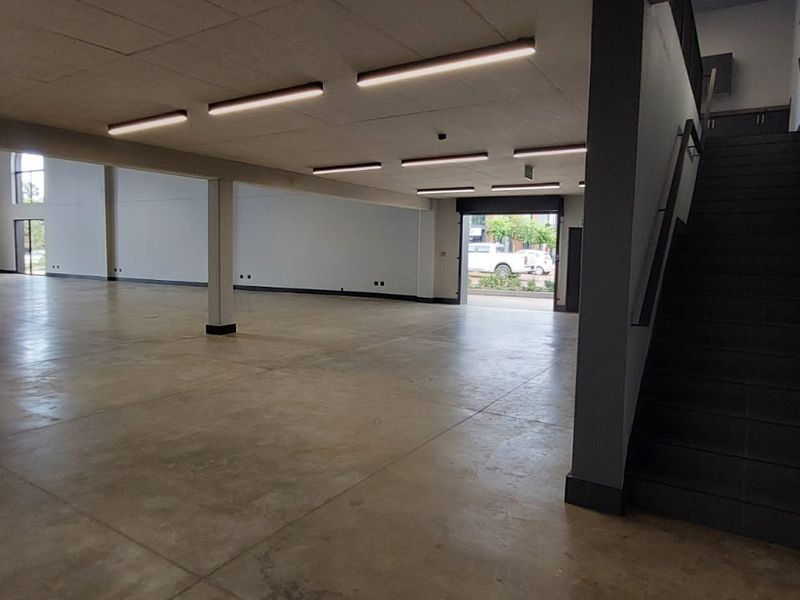 Spacious open-plan retail area featuring polished concrete flooring, modern linear lighting, and a dedicated staircase leading to an upper level.
