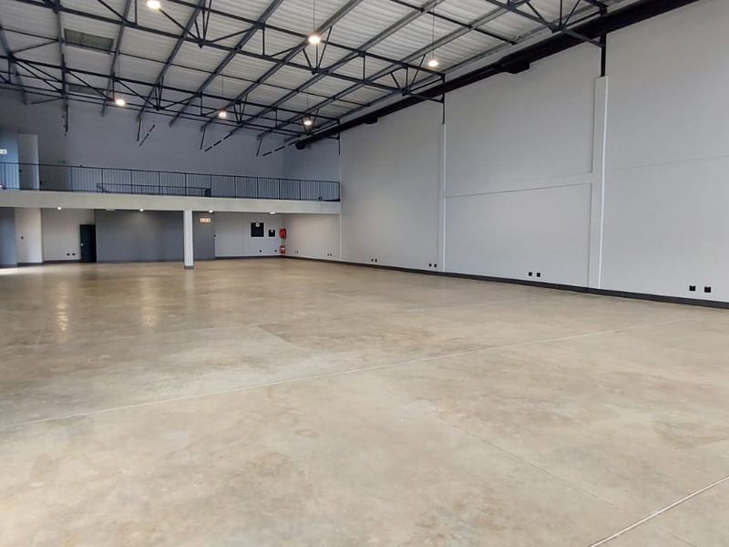 Spacious open-plan retail or industrial unit featuring high ceilings, polished concrete flooring, and a mezzanine level with safety railing.