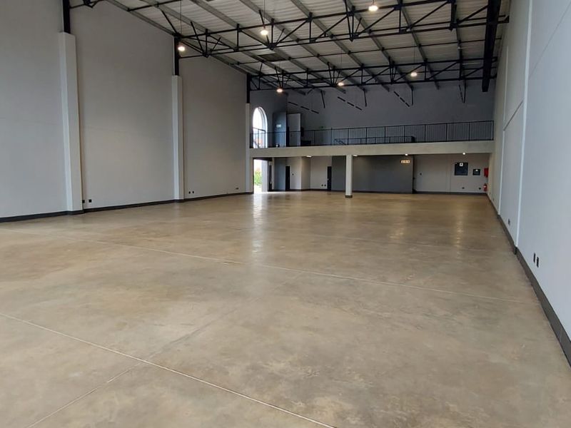 Spacious open-plan retail or industrial unit featuring high ceilings, polished concrete flooring, and a mezzanine level with metal railings.