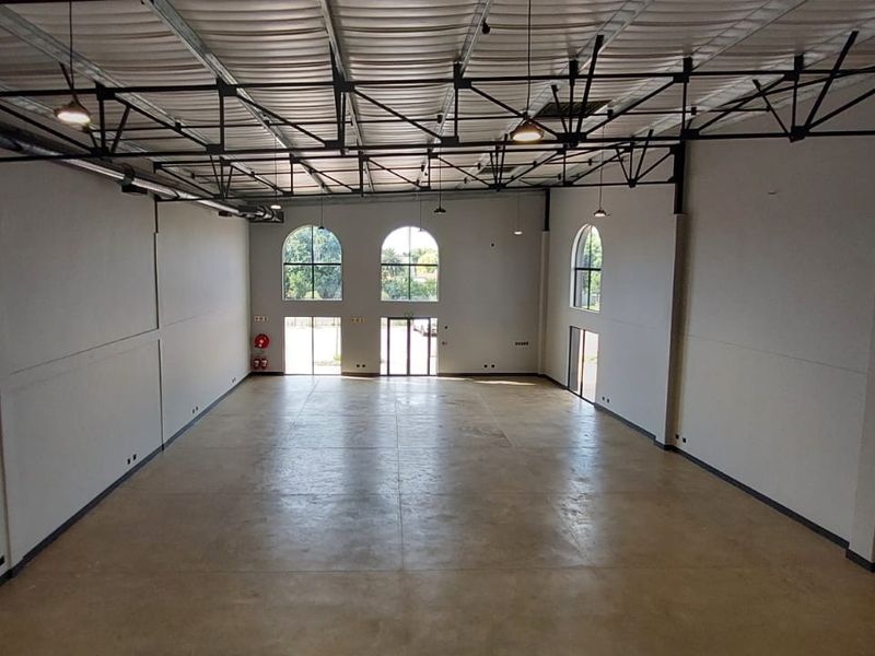 Spacious open-plan retail or commercial unit featuring high exposed truss ceilings, polished concrete flooring, and large arched windows providing ample natural light.