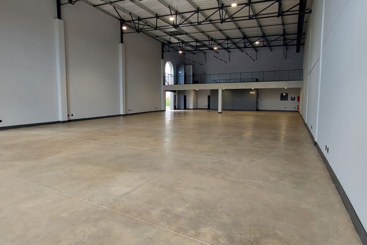 Spacious open-plan retail or industrial unit featuring high ceilings, polished concrete flooring, and a mezzanine level with metal railings.