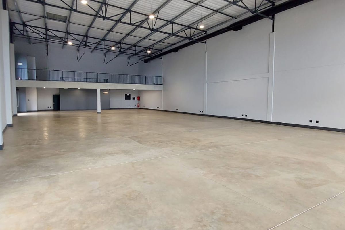 Spacious open-plan retail or industrial unit featuring high ceilings, polished concrete flooring, and a mezzanine level with safety railing.