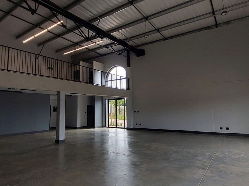 Spacious open-plan retail or industrial unit featuring high ceilings, polished concrete flooring, a mezzanine level with metal railing, and large windows for natural light.