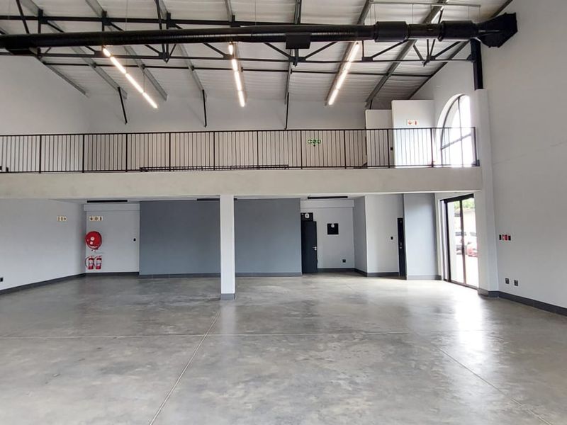 Spacious open-plan retail unit featuring high ceilings, exposed industrial ducting, polished concrete flooring, and a mezzanine level with metal railing.