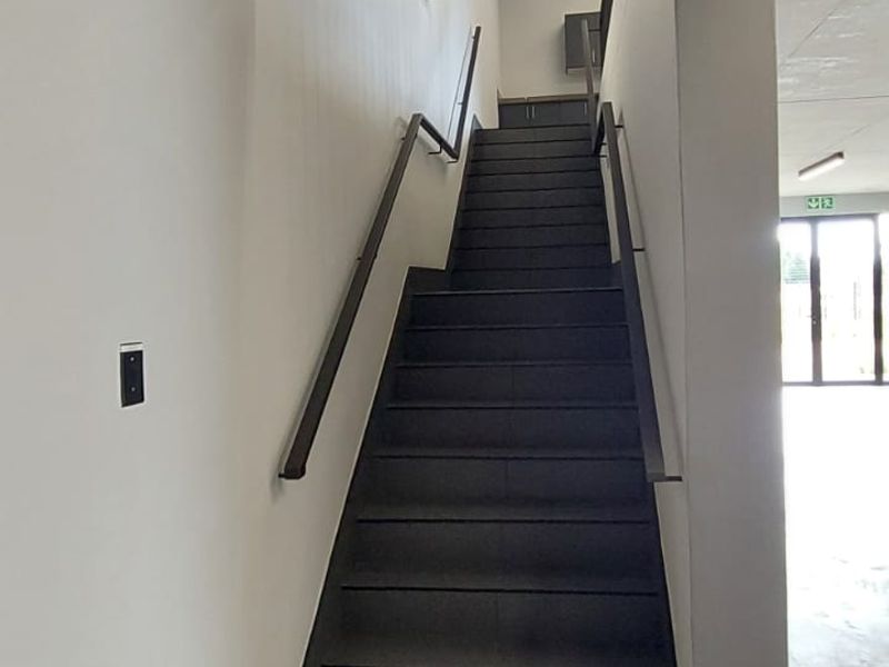 A modern interior staircase featuring dark tiled steps, sleek handrails, and a minimalist design within a commercial retail space.