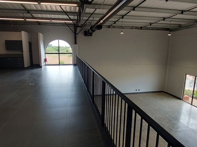 Spacious mezzanine level in a retail unit featuring tiled flooring, metal railings, exposed industrial ceiling, and a small kitchenette area.