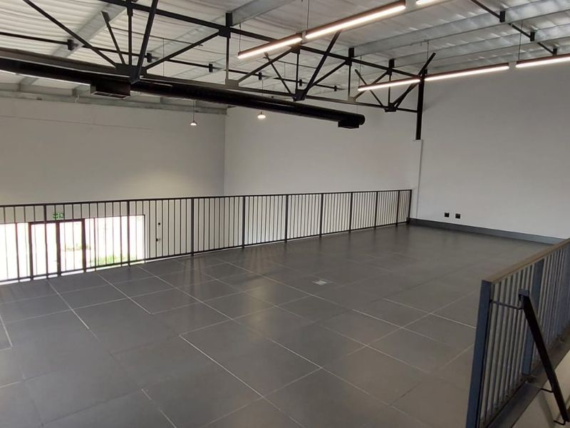 Spacious mezzanine level featuring tiled flooring, industrial-style exposed ceiling trusses, modern linear lighting, and a secure metal balustrade overlooking the lower level.