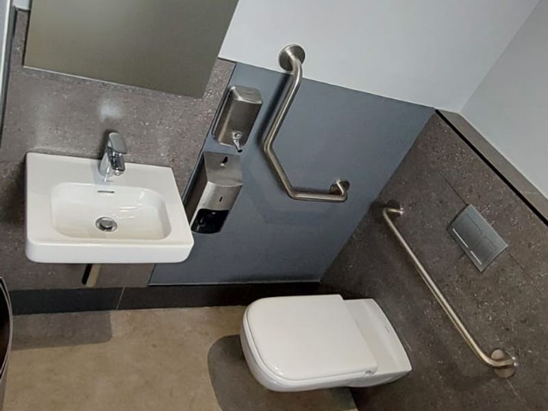 Accessible restroom featuring a wall-mounted basin, wall-hung toilet, and stainless steel grab rails with modern tiled finishes.