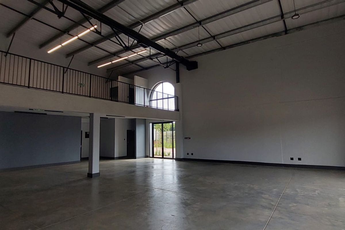 Spacious open-plan retail or industrial unit featuring high ceilings, polished concrete flooring, a mezzanine level with metal railing, and large windows for natural light.