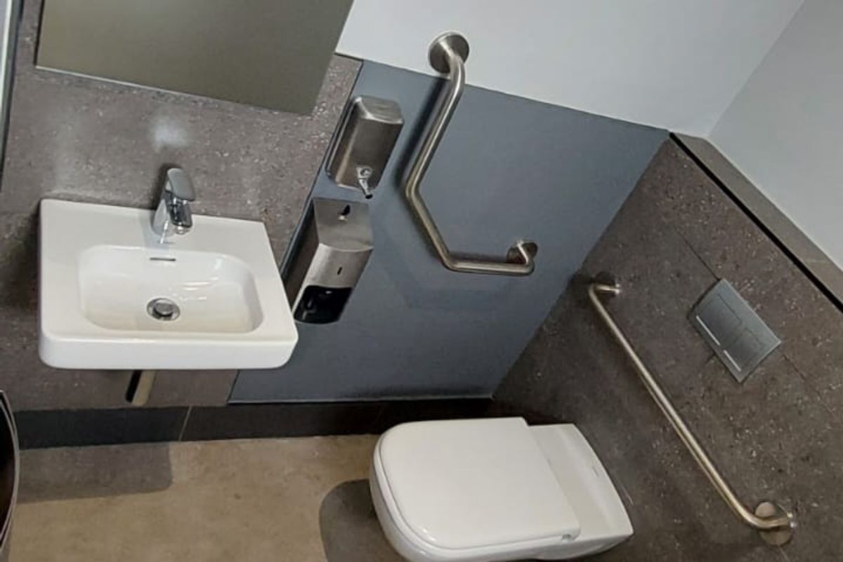 Accessible restroom featuring a wall-mounted basin, wall-hung toilet, and stainless steel grab rails with modern tiled finishes.