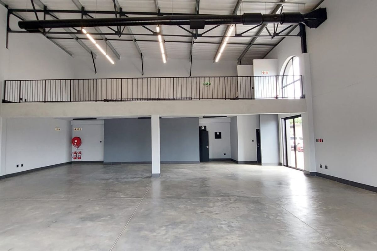 Spacious open-plan retail unit featuring high ceilings, exposed industrial ducting, polished concrete flooring, and a mezzanine level with metal railing.