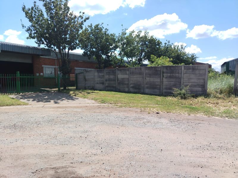 Exterior view of a commercial property featuring a gated entrance, brick warehouse structure, and a concrete perimeter boundary wall.