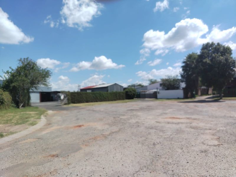 An expansive view of the vacant commercial land, featuring an unpaved gravel surface and surrounding perimeter hedging.