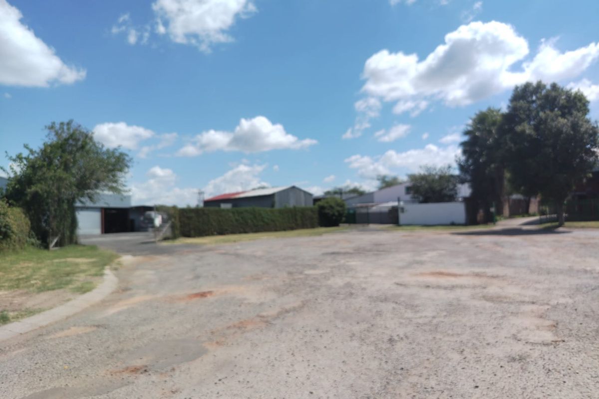An expansive view of the vacant commercial land, featuring an unpaved gravel surface and surrounding perimeter hedging.