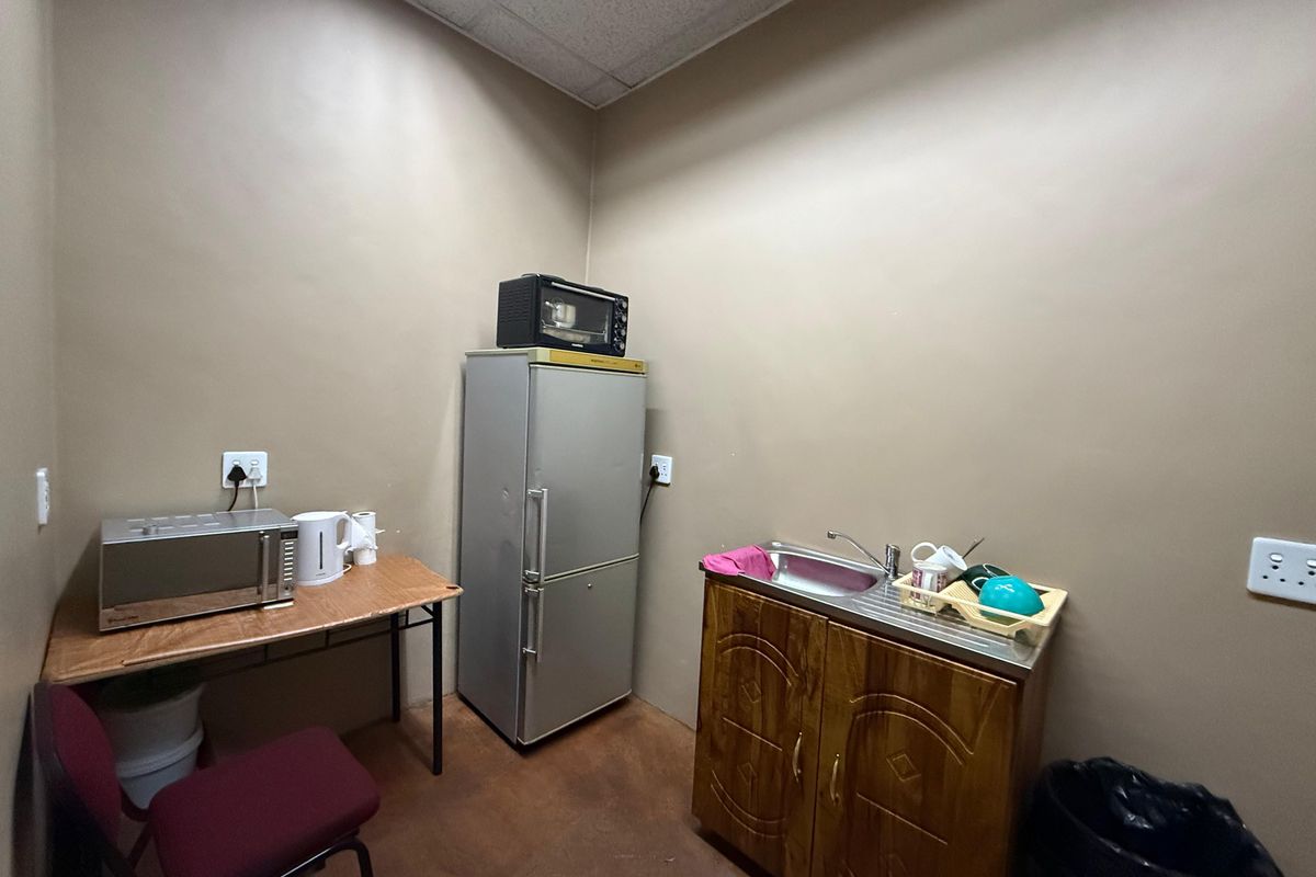 A functional industrial kitchenette featuring a stainless steel sink, wooden base cabinetry, and drop ceiling lighting, suitable for staff break area use.