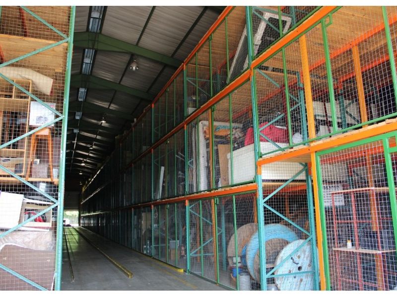 Industrial storage facility featuring multi-level wire mesh cages and heavy-duty steel racking systems within a large warehouse space.