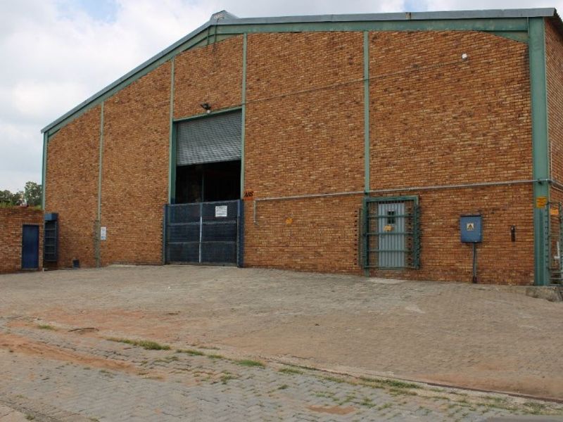 Industrial warehouse exterior featuring a large brick facade, roller shutter door access, and a paved yard area with security fencing.