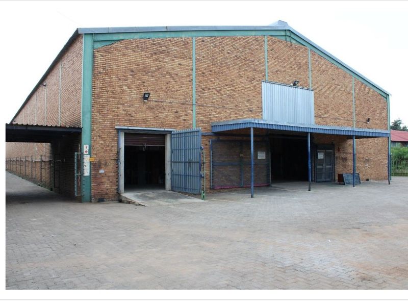 Industrial warehouse facility featuring a brick facade, steel frame construction, multiple roller shutter access points, and a paved yard area for loading.