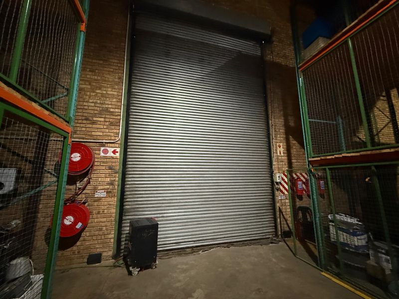 Industrial warehouse space featuring a large roller shutter door, exposed brick walls, and integrated fire safety equipment including hose reels and extinguishers.