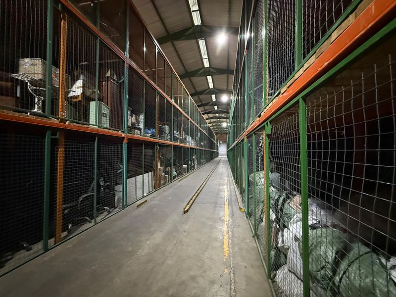 Industrial storage facility featuring high-density wire mesh partitioned racking units, concrete flooring, and exposed steel roof structure with overhead lighting.