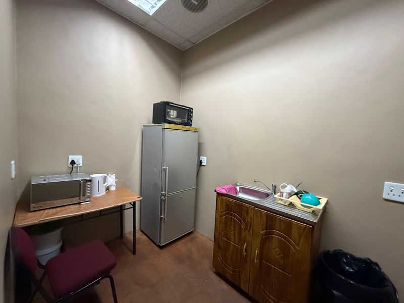A functional industrial kitchenette featuring a stainless steel sink, wooden base cabinetry, and drop ceiling lighting, suitable for staff break area use.