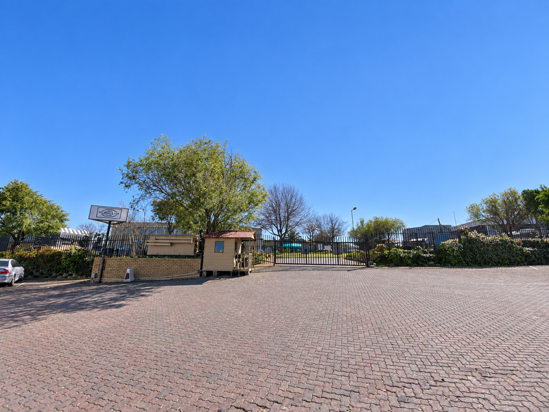 Industrial property entrance featuring a paved driveway, secure perimeter fencing, and a dedicated guard booth for controlled access.