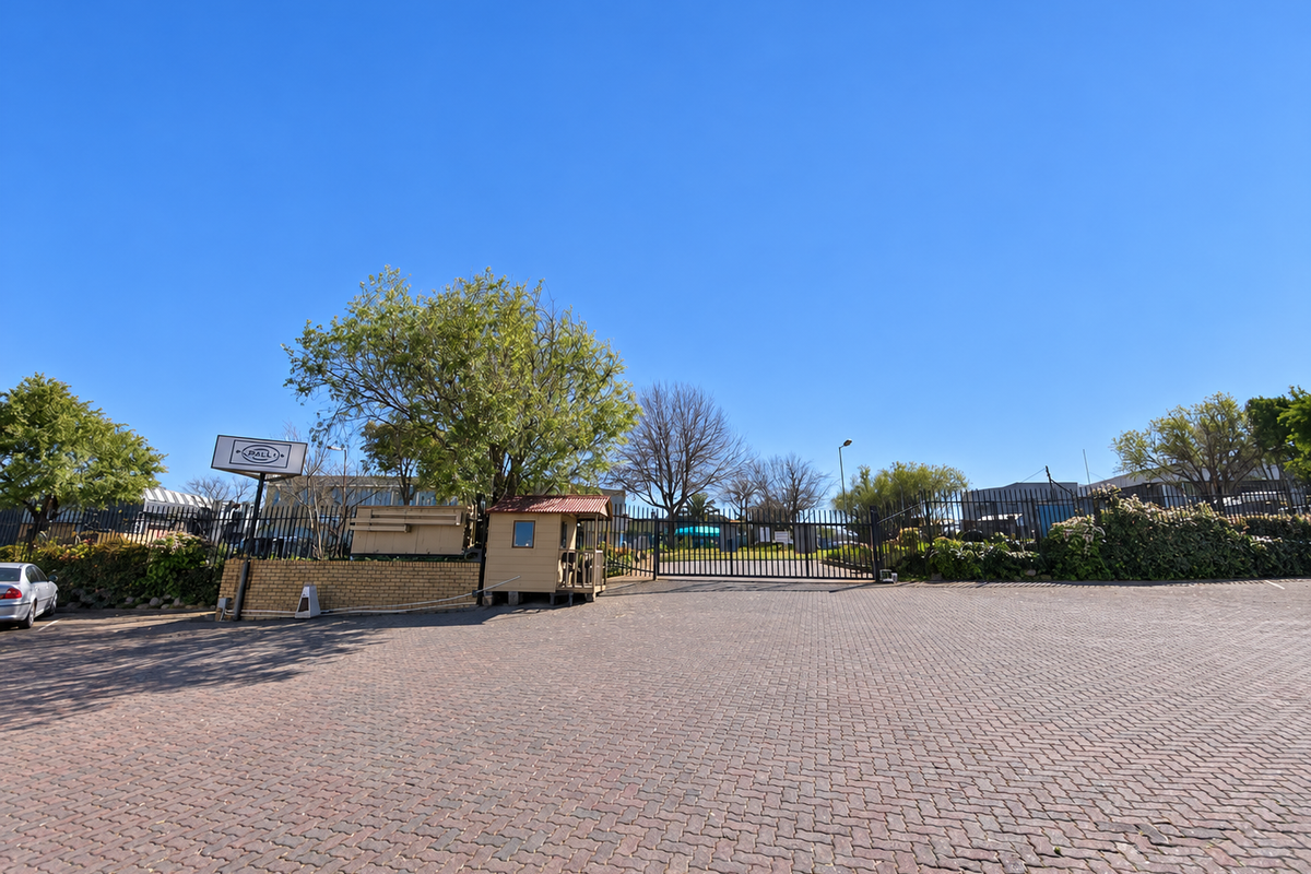 Industrial property entrance featuring a paved driveway, secure perimeter fencing, and a dedicated guard booth for controlled access.