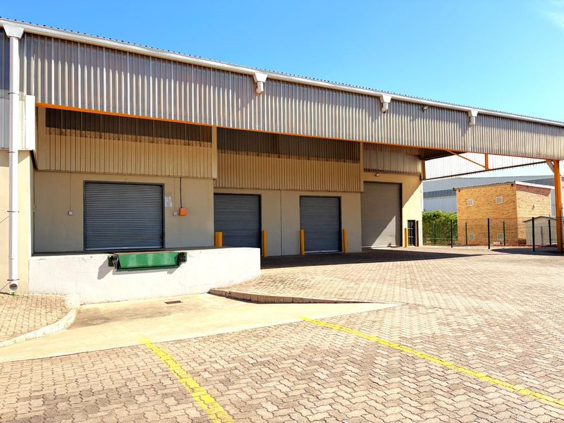 Industrial warehouse exterior featuring multiple roller shutter doors, a dedicated loading dock with a dock leveler, and a spacious paved yard area.