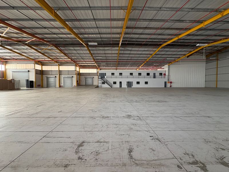 Spacious industrial warehouse featuring high ceilings, steel portal frame construction, multiple roller shutter doors, and an integrated two-level office block.