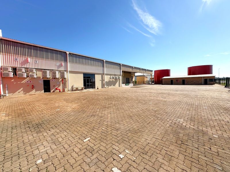 Spacious industrial yard featuring paved surfacing, metal-clad warehouse exterior, multiple air conditioning units, and large storage tanks.