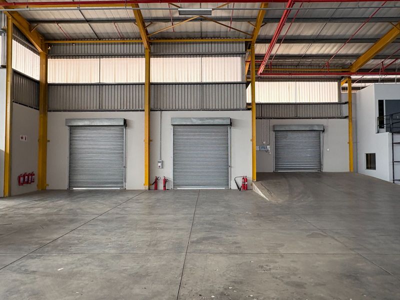 Spacious industrial warehouse interior featuring three roller shutter doors, concrete flooring, exposed steel beams, and integrated fire safety systems.