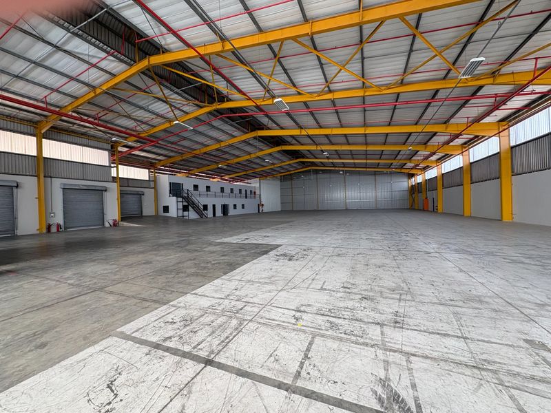 Expansive industrial warehouse space featuring high ceilings, steel portal frame construction, roller shutter access, and an integrated mezzanine office level.